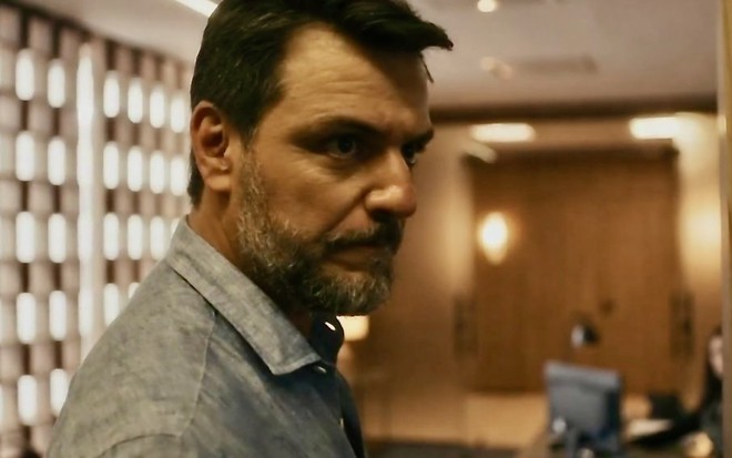 O ator Rodrigo Lombardi faz uma expressão de raiva em cena da novela Travessia na qual usa camisa jeans como Moretti