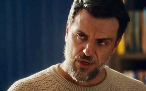 O ator Rodrigo Lombardi usa uma blusa bege e faz uma expressão de fúria em cena de Travessia como o personagem Moretti