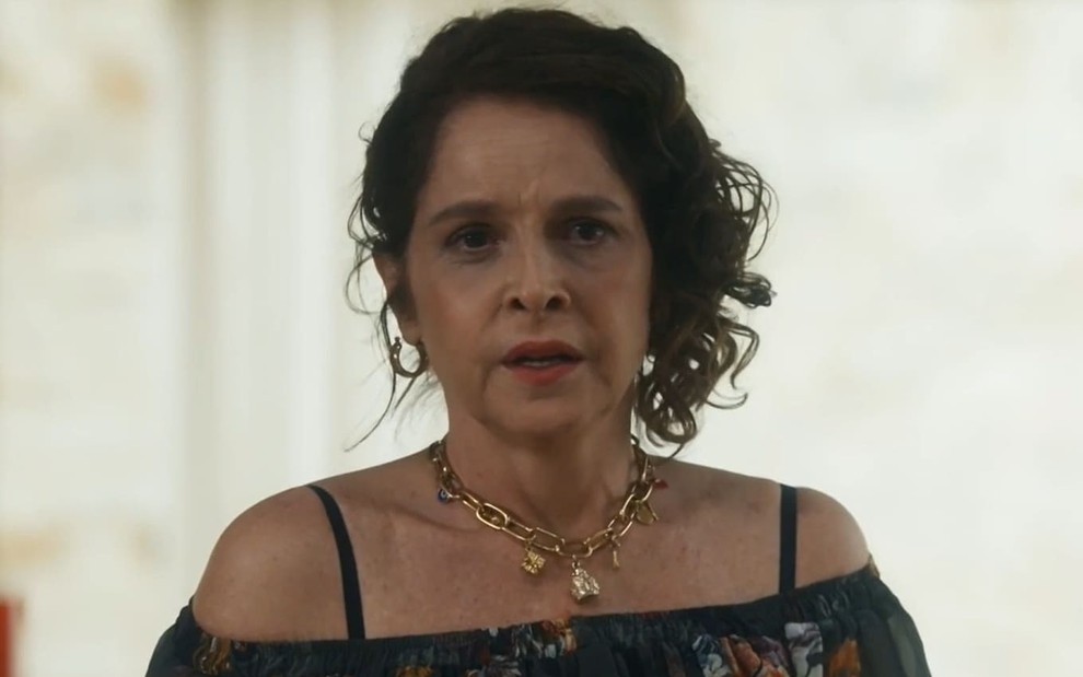 Drica Moraes caracterizada como Núbia em Travessia; ela usa um vestido azul e tem o semblante preocupado em cena da novela