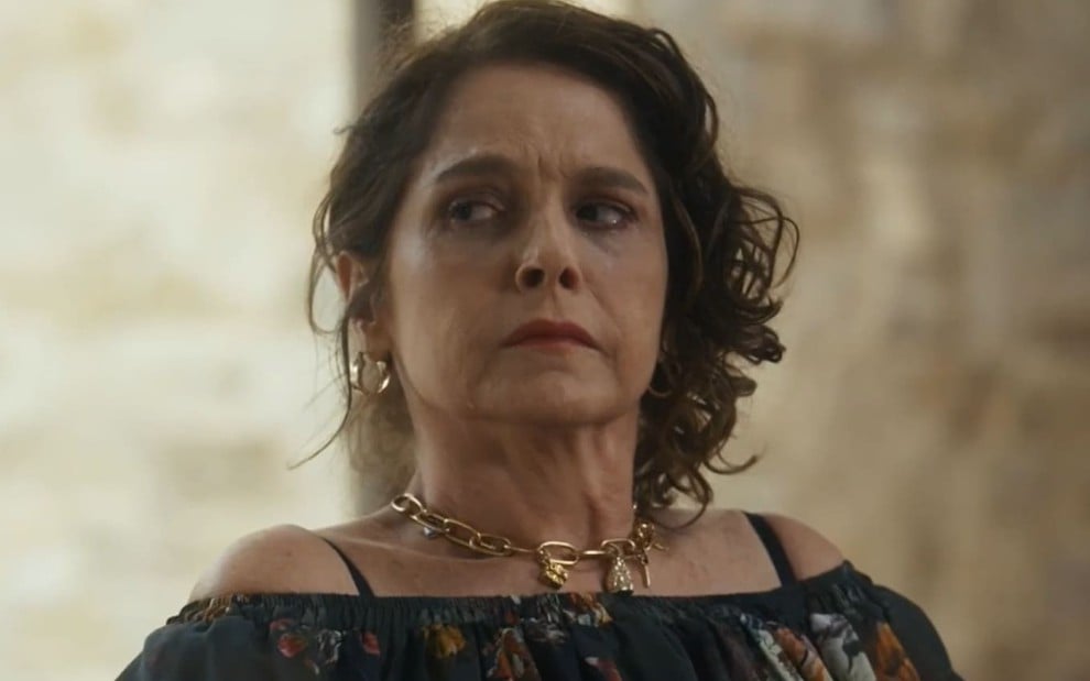 Drica Moraes caracterizada como Núbia em Travessia; ela usa uma blusa preta e tem a expressão debochada em cena da novela