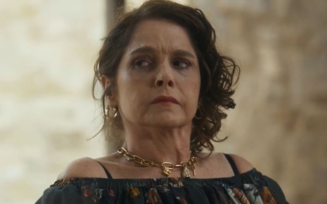Drica Moraes caracterizada como Núbia em Travessia; ela usa uma blusa preta e tem a expressão debochada em cena da novela