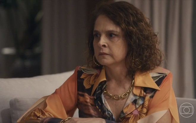 A atriz Drica Moraes está séria e usa blusa com estampa colorida em cena de Travessia como a personagem Núbia