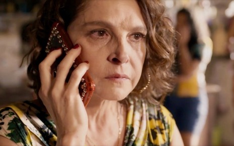 A atriz Drica Moraes está simulando conversa pelo celular enquanto chora em cena da novela Travessia como Núbia