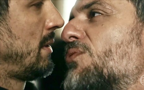 Os atores Romulo Estrela e Rodrigo Lombardi estão com os rostos quase colados e em close em cena da novela Travessia