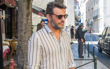 Rodrigo Lombardi usa uma camisa social listrada e um óculos escuro em cena de Travessia