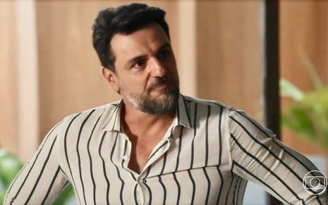 O ator Rodrigo Lombardi faz uma expressão de deboche em cena da novela Travessia na qual usa uma blusa listrada
