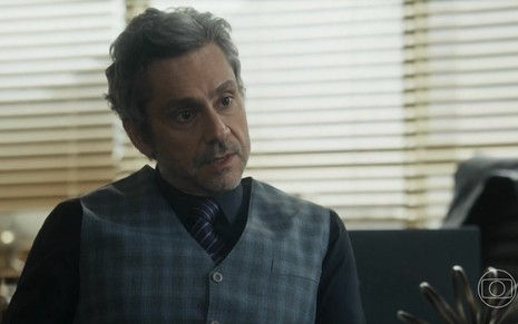 O ator Alexandre Nero usa colete, gravata e camisa escura em cena de Travessia como o advogado Stenio