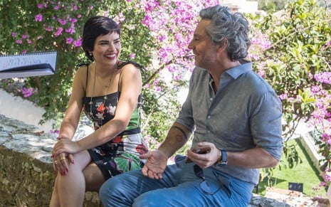 Vanessa Giácomo e Alexandre Nero conversam, sorridentes, na frente de um campo florido