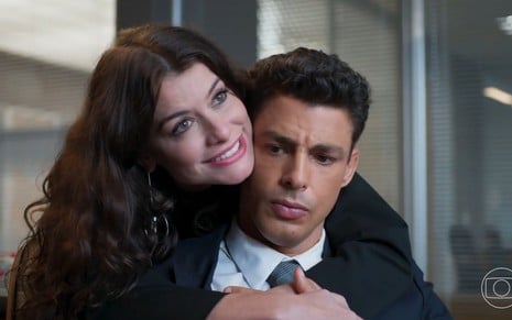 Bárbara (Alinne Moraes) abraça Christian/Renato (Cauã Reymond) por trás, e ele faz cara de reprovação em cena de Um Lugar ao Sol