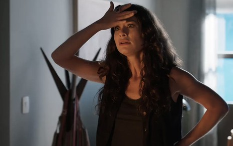 A atriz Alinne Moraes leva a mão direita à testa, em sinal de preocupação, como a Bárbara em cena de Um Lugar ao Sol