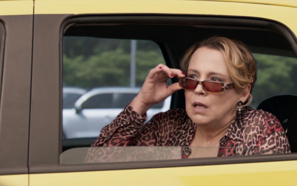 A atriz Ana Beatriz Nogueira como Elenice abaixa os óculos escuros, com cara de espanto, dentro de um táxi em cena de Um Lugar ao Sol