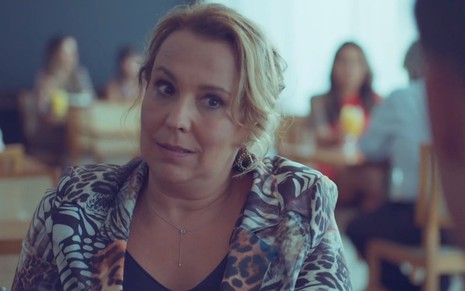 Elenice (Ana Beatriz Nogueira) está sentada em mesa de restaurante em cena de Um Lugar ao Sol