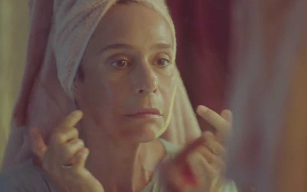 A atriz Andrea Beltrão com uma toalha na cabeça, cutuca o rosto com os dedos, como a Rebeca em cena de Um Lugar ao Sol