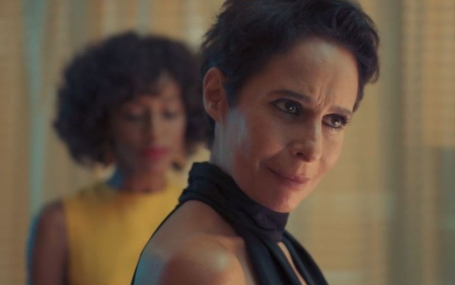 Rebeca (Andrea Beltrão) está em pé no banheiro, Ruth (Pathy Dejesus) está atrás dela em cena de Um Lugar ao Sol