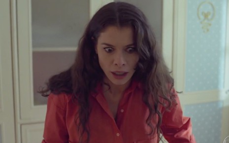Alinne Moraes em cena de Um Lugar ao Sol: atriz está de camisa laranja, olha para baixo com expressão de desespero