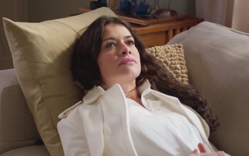 Alinne Moraes em cena de Um Lugar ao Sol: deitada, atriz está com os cabelos soltos, roupas brancas e olha para cima