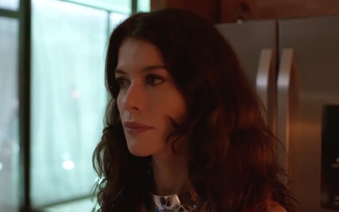 Alinne Moraes em cena de Um Lugar ao Sol: em close, atriz está com os cabelos soltos e olha com desaprovação para alguém fora do quadro