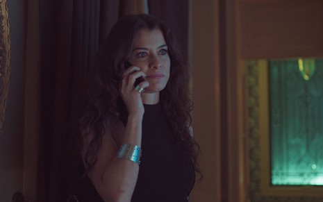 Alinne Moraes grava vestida de preto, joias prateadas e ao telefone como Bárbara de Um Lugar ao Sol