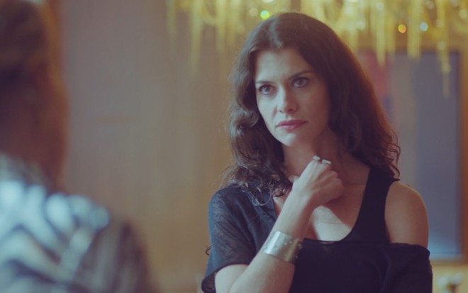 Alinne Moraes grava com cabelo cacheado, roupa preta e expressão séria como Bárbara de Um Lugar ao Sol