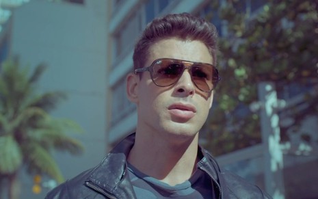 O ator Cauã Reymond usa óculos escuros e jaqueta em cena diurna de Um Lugar ao Sol, novela das nove da Globo