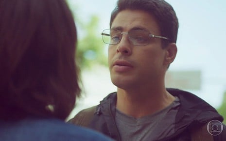 Christian (Cauã Reymond)  usa óculos e conversa na rua com Lara (Andréia Horta), que está de costas na foto, em cena de Um Lugar ao Sol