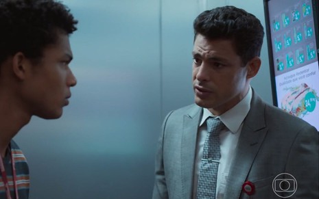 Christian (Cauã Reymond) e Ravi (Juan Paiva) estão em elevador em cena de Um Lugar ao Sol