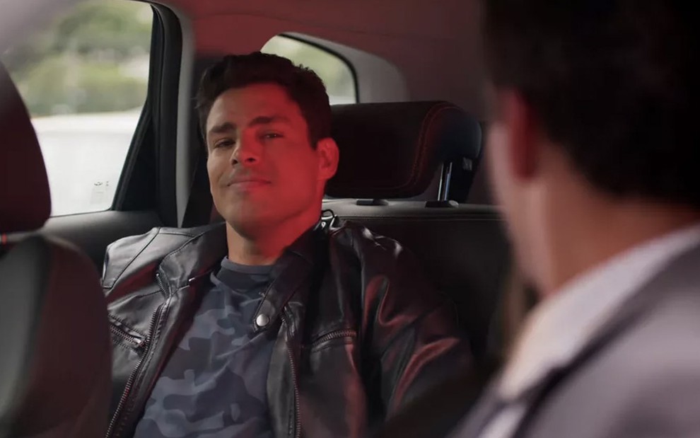 O ator Cauã Reymond como o Renato dentro de um carro, com um sorriso cínico, em cena de Um Lugar ao Sol