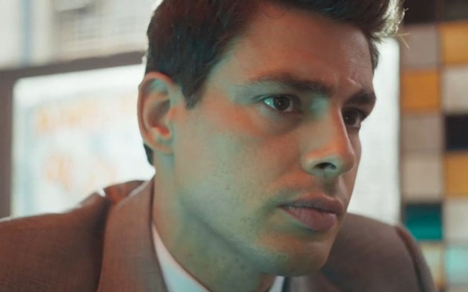 Christian (Cauã Reymond) está sentado em mesa de bar em cena de Um Lugar ao Sol