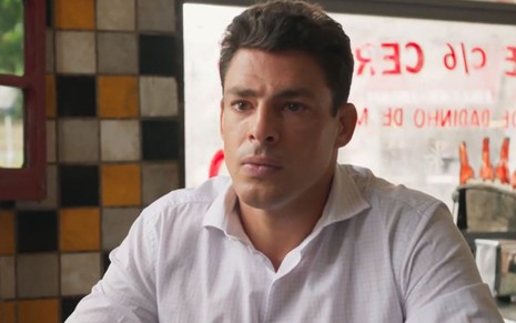 Christian (Cauã Reymond) está sentado em mesa de bar em cena de Um Lugar ao Sol, novela das nove da Globo
