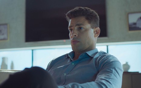 O ator Cauã Reymond faz uma expressão de seriedade em gravação de cena de Um Lugar ao Sol na qual ele está com uma camisa azul