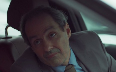 O ator Daniel Dantas se curva em um carro para falar com alguém do lado de fora do veículo em cena de Um Lugar ao Sol
