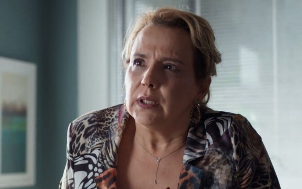 Ana Beatriz Nogueira em cena de Um Lugar ao Sol: atriz está caracterizada como Elenice, sentada e olha indignada para alguém fora do quadro