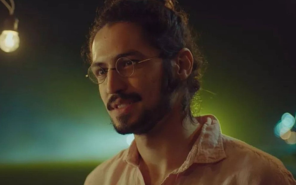 Felipe (Gabriel Leone) está de cabelo preso e usa óculos em cena de Um Lugar ao Sol