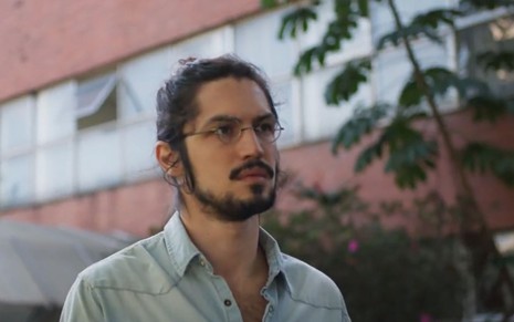 Felipe (Gabriel Leone) está de cabelo preso e usa óculos em cena de Um Lugar ao Sol
