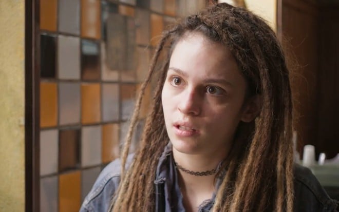 Joy (Lara Tremouroux) está sentada em mesa de bar em cena de Um Lugar ao Sol