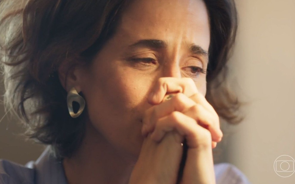 Ilana (Mariana Lima) está com as mãos cruzadas e chora em cena de Um Lugar ao Sol