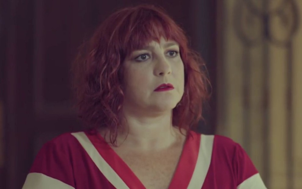 Ana Baird em cena de Um Lugar ao Sol: atriz está caracterizada como Nicole, vestido vermelho com detalhes em branco e olha com espanto para alguém fora do quadro