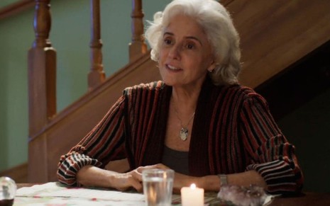 Marieta Severo, caracterizada como Noca, se apoia em mesa com cartas de tarô em cena de Um Lugar ao Sol