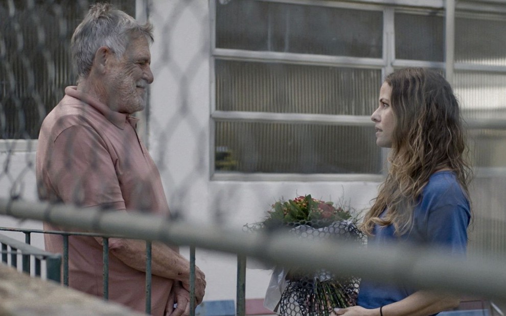 José de Abreu e Fernanda de Freitas em cena de Um Lugar ao Sol: ator está de camiseta vermelha e olha para atriz, que segura buquê e segura camisa azul