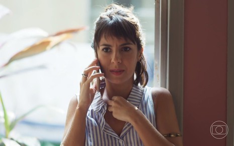 A atriz Andréia Horta fala ao telefone e mexe em uma corrente em seu pescoço durante gravação de cena como Lara de Um Lugar ao Sol