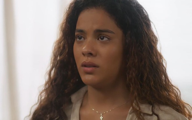Bella Campos caracterizada como Jenifer; ela tem o semblante apreensivo em cena de Vai na Fé