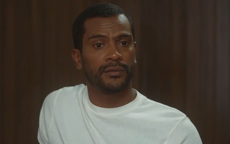 Samuel de Assis em cena de Vai na Fé; ator tem o semblante sério e usa uma camiseta branca