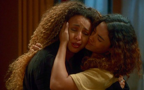 As atrizes Sheron Menezzes e Bella Campos abraçadas, Sheron com expressão de choro e Bella a consolando, em cena de Vai na Fé