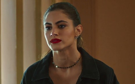 Érika (Leticia Salles) com expressão séria em cena de Vai na Fé; ela usa roupas pretas e batom vermelho