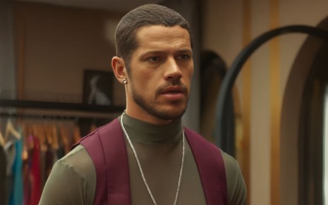 José Loreto caracterizado como Lui Lorenzo em Vai na Fé; ele usa uma camiseta verde e um colete vermelho e está sério em cena de Vai na Fé