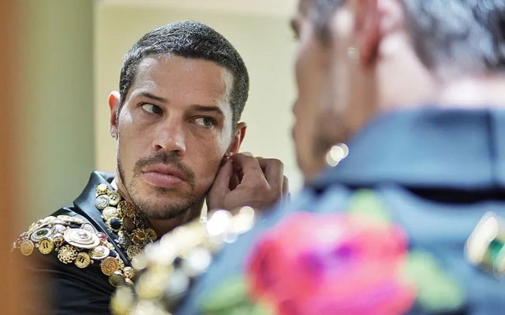 O ator José Loreto coloca brinco na orelha diante de um espelho em cena da novela Vai na Fé como Lui Lorenzo