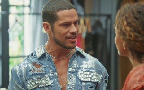 José Loreto caracterizado como Lui Lorenzo em Vai na Fé; ele está com uma camisa jeans e dá um sorriso sedutor em cena da novela