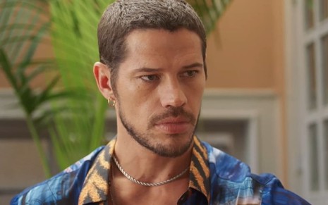 José Loreto caracterizado como Lui Lorenzo em Vai na Fé; ele está com uma camisa jeans e tem o semblante sério em cena da novela