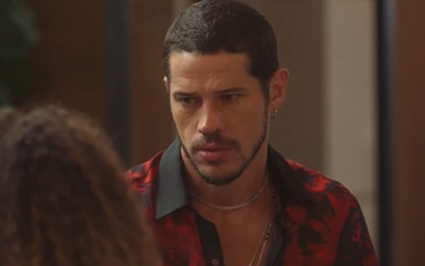 José Loreto caracterizado como Lui Lorenzo em Vai na Fé; ele está com uma camisa listrada e parece cabisbaixo em cena da novela