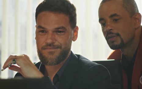 O ator Emilio Dantas contracena com Jonathan Haagensen em Vai na Fé, ambos olham para algo na tela de um computador